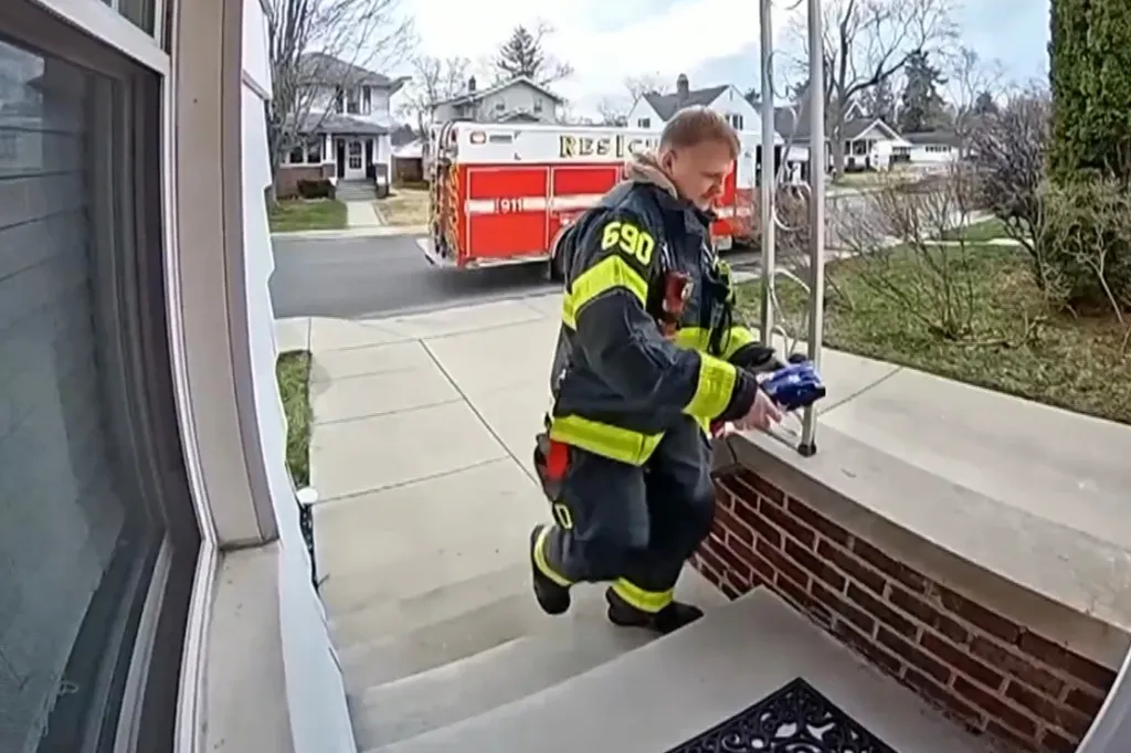 A firefighter in uniform holding a folded American flag walking up steps to a house, with a rescue truck in the background.