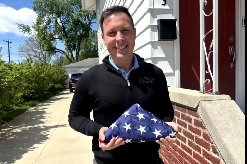 A man holding a neatly folded American flag in front of a house.