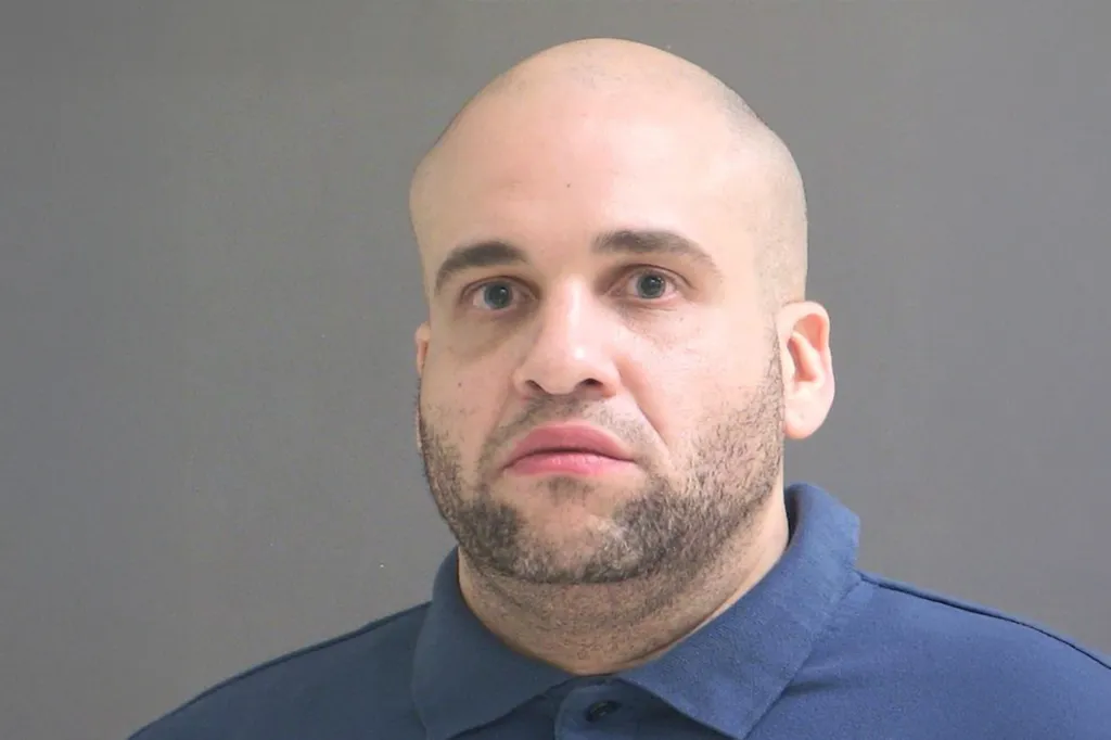 Mugshot of a bald man with a beard wearing a blue polo shirt.