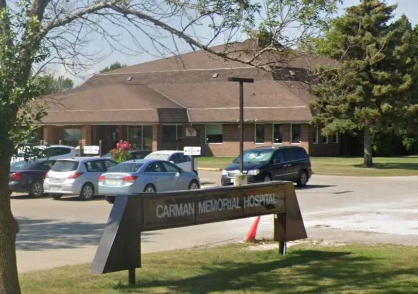 Exterior of Carman Memorial Hospital with a brown roof and cars parked in front.