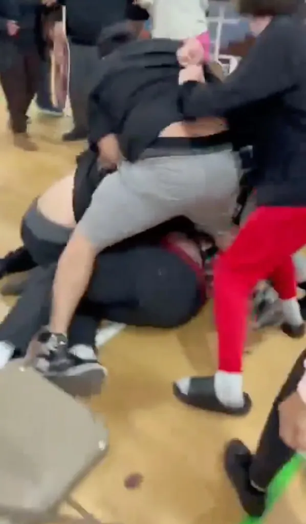Several people are fighting on a wooden floor, with one person pinned beneath the others.