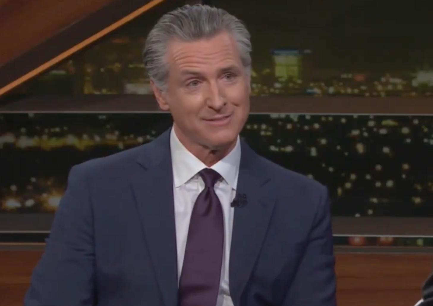 Gavin Newsom smiling and looking at a man in a black suit.
