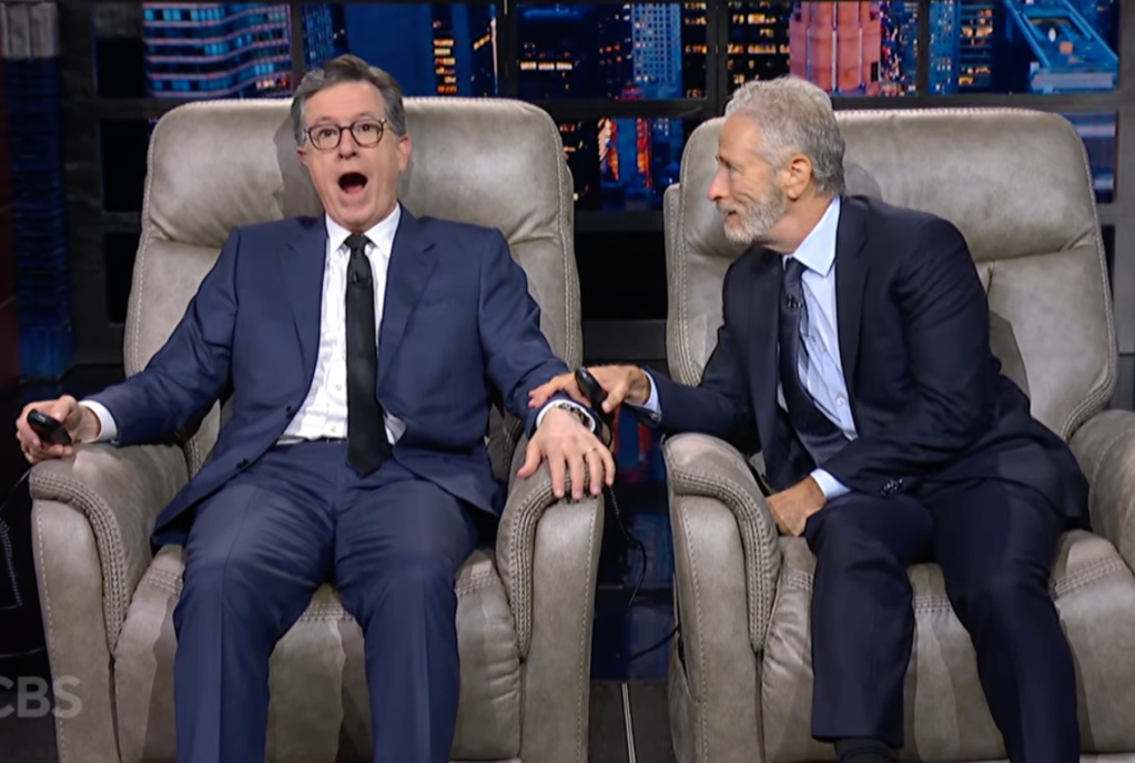 Stephen Colbert looks surprised as Jon Stewart grasps his arm.