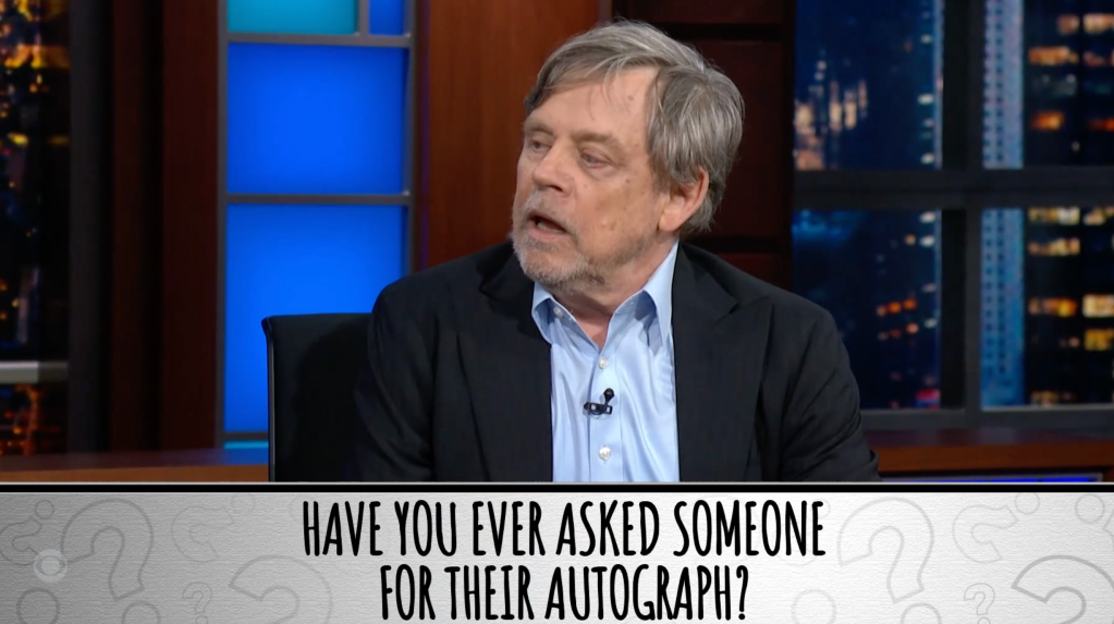 Mark Hamill in a blue shirt and dark jacket in a TV studio, with text below asking
