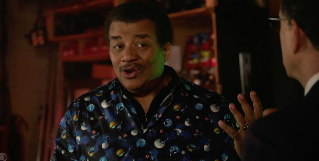 Neil deGrasse Tyson speaking to a man in a dark room.