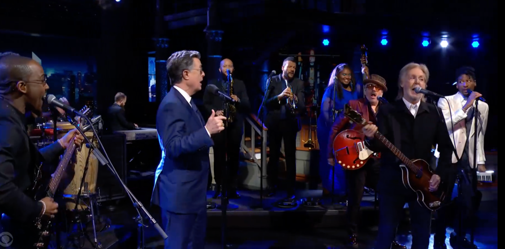 Stephen Colbert singing with musicians on stage.