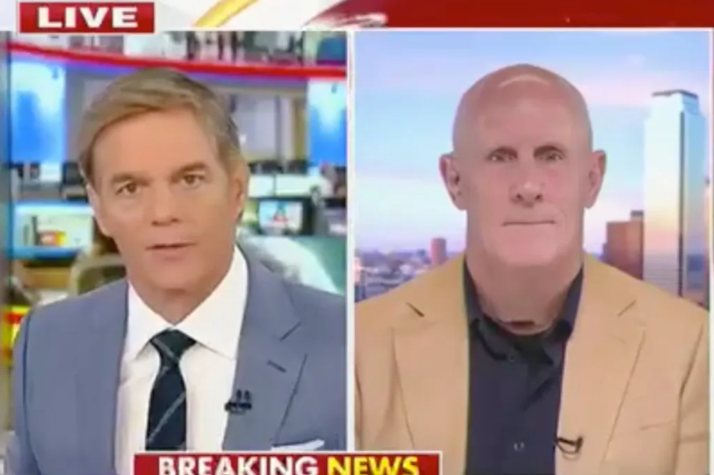A split screen showing a news anchor in a suit on the left and a bald man in a tan jacket on the right.