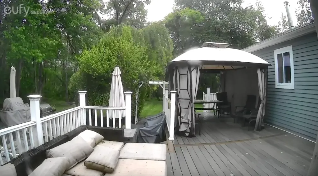 A backyard deck with a gazebo, patio furniture, and a grill, surrounded by trees.