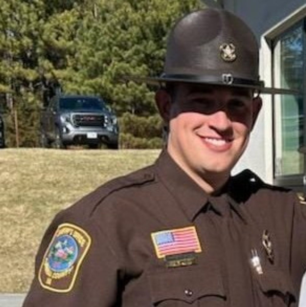 A smiling police officer in uniform and a brown hat.