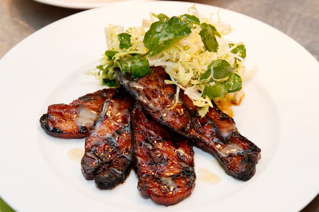 Glazed pork belly slices with a side of frisée and watercress salad.