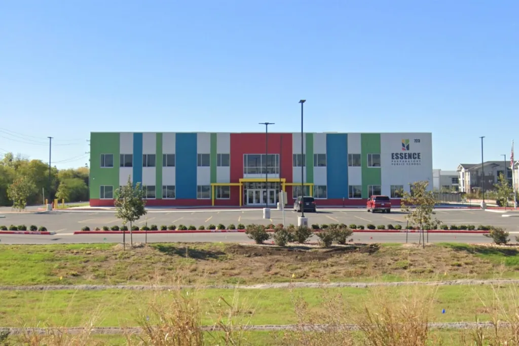 Essence Preparatory Public School building, featuring colorful stripes of green, white, blue, and red, with a parking lot in front.