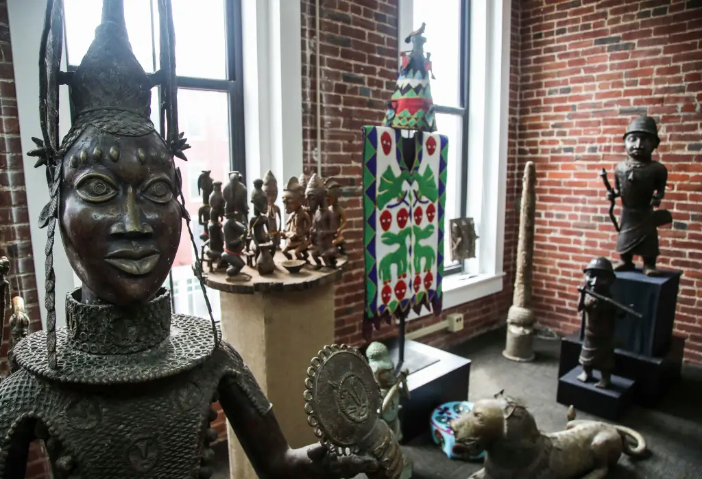 A display of Nigerian art, including a bronze head of a woman with a tall, winged headdress, and smaller figures.