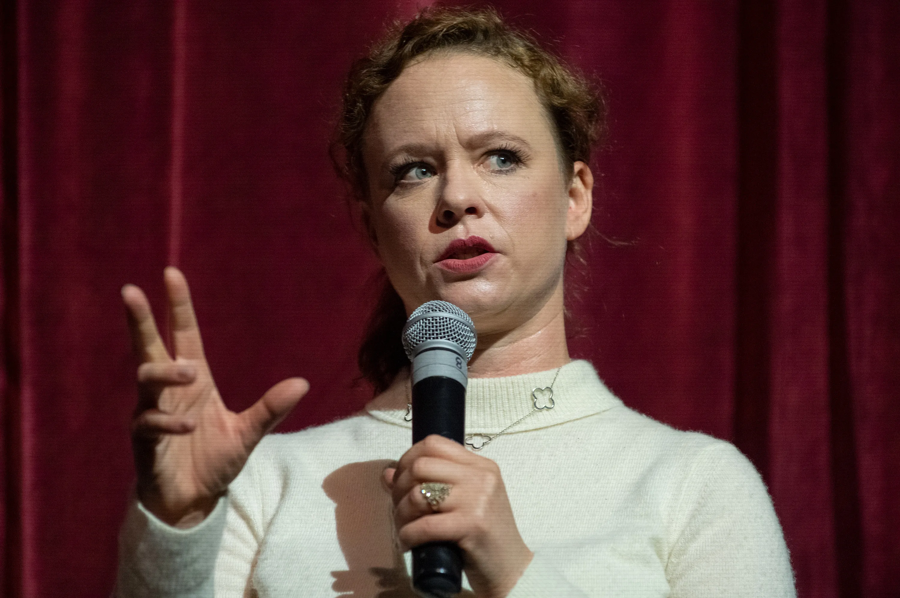Thora Birch speaks on stage holding a microphone.
