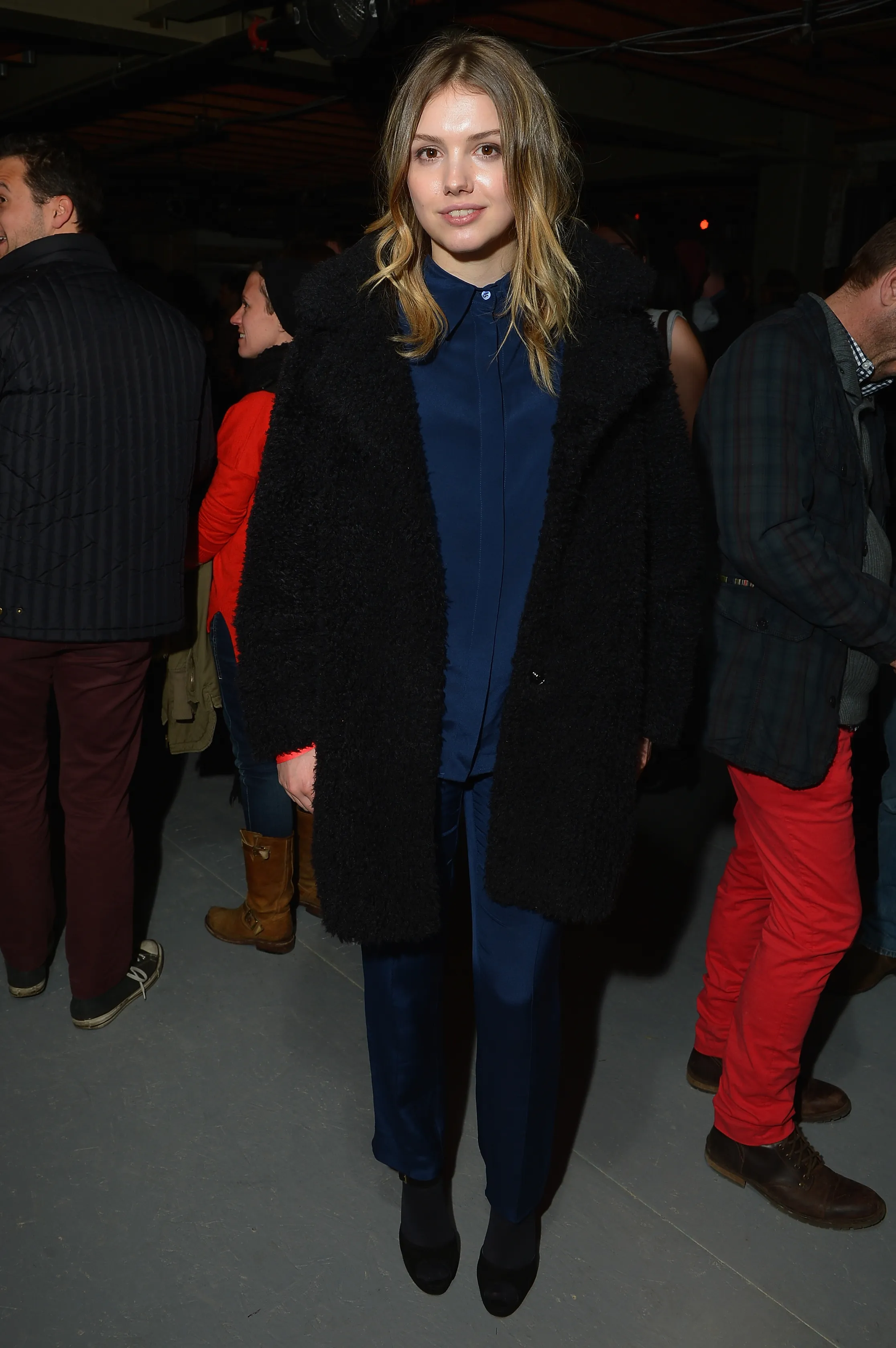 Actress Hannah Murray wearing a black coat over a blue shirt and pants.