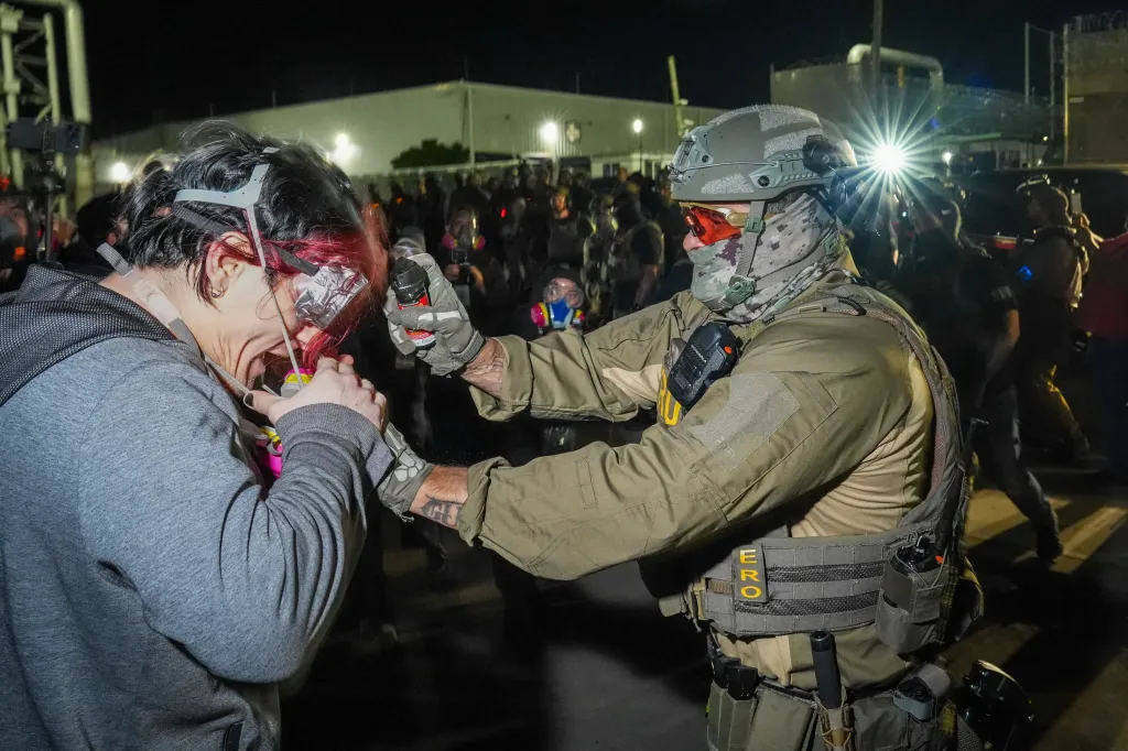 An ERO agent sprays pepper spray into the mask of a protester during a clash outside Delaney Hall on May 28, 2026.