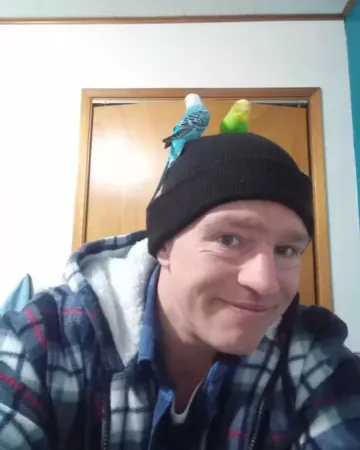 Matt Brown wearing a black beanie with two parakeets perched on top.