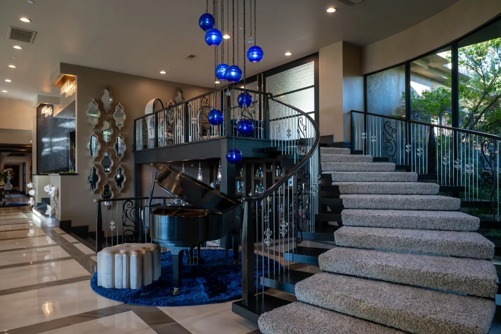 Grand entry foyer with a large staircase, shiny tile floors, and a grand piano underneath a multi-colored chandelier.