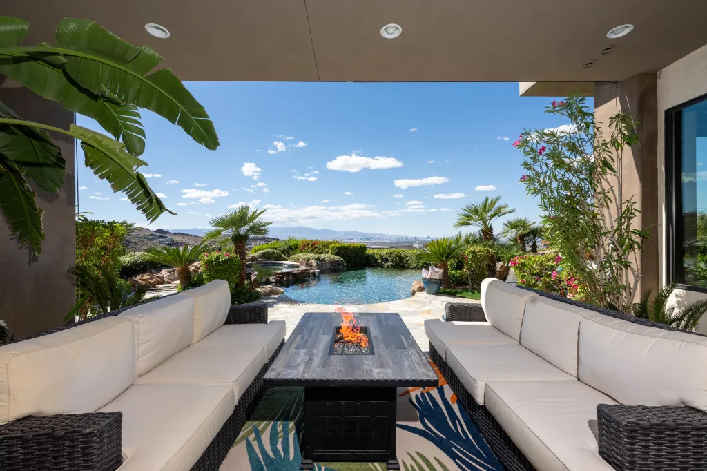 Covered patio with a fire pit, two sofas, an infinity pool, and a view of mountains and the city in the distance.