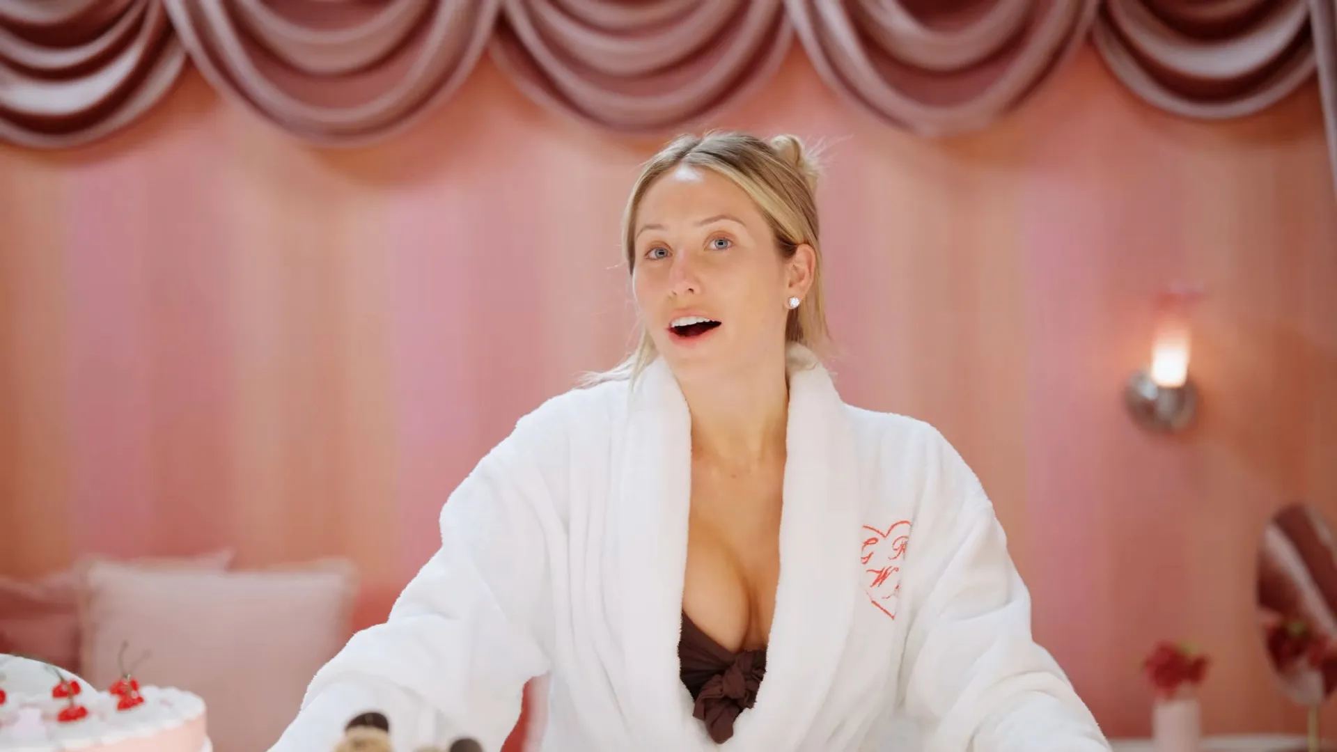 Alix Earle in a white robe with an open mouth expression.