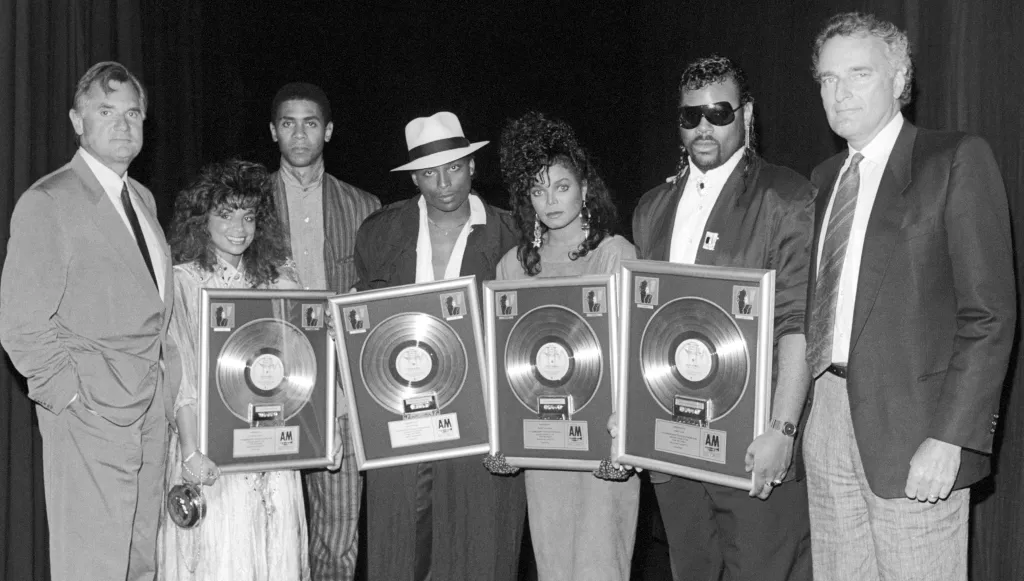 Black and white photo of seven people, including Paula Abdul and Janet Jackson, holding framed records for the album 