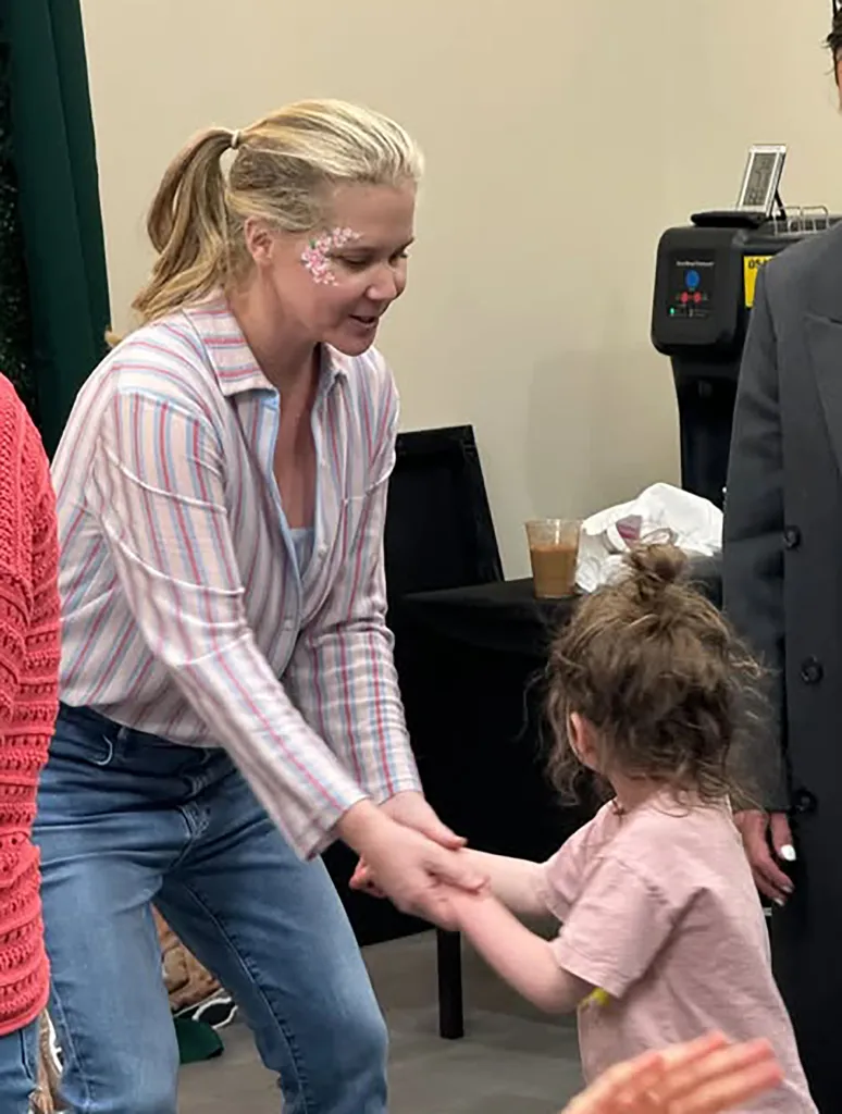 Amy Schumer playing with a child, with flower face paint on her cheek.