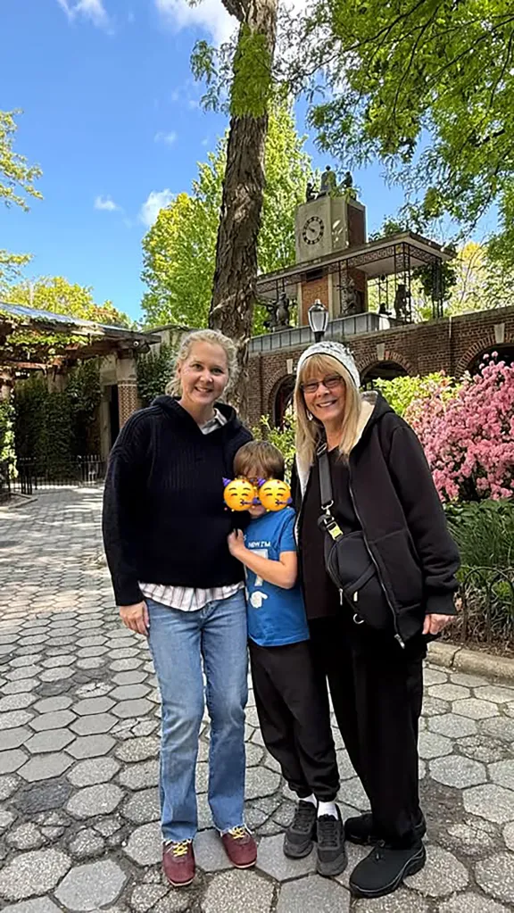 Amy Schumer and a woman pose with a child whose face is covered by emojis.