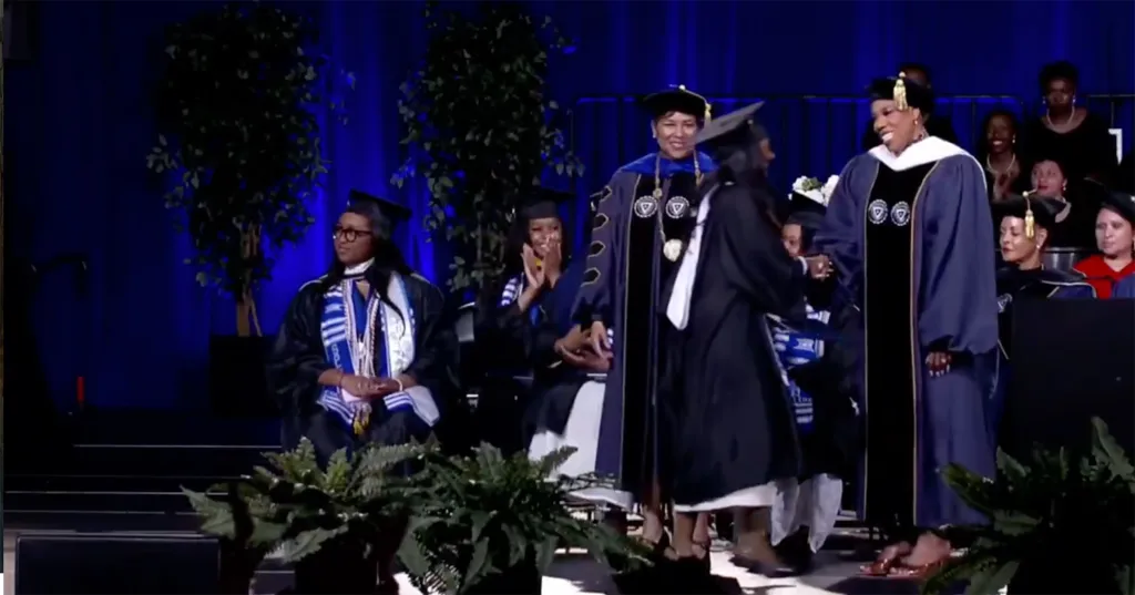 Zahara Jolie-Pitt shaking hands with a woman in academic regalia at a graduation ceremony.