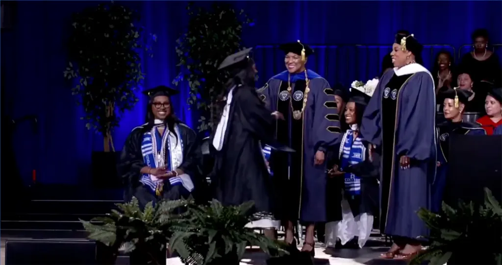 Zahara Jolie-Pitt shaking hands with a woman in academic regalia at her graduation ceremony.