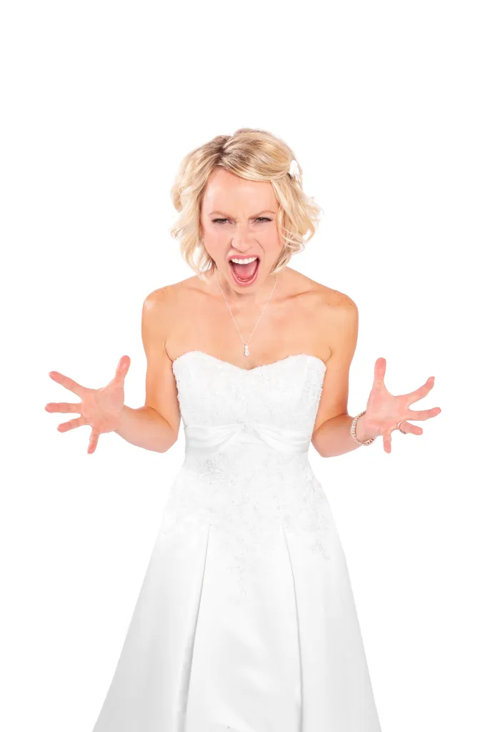 A young, angry blonde bride in a white wedding dress yells with her hands splayed out.