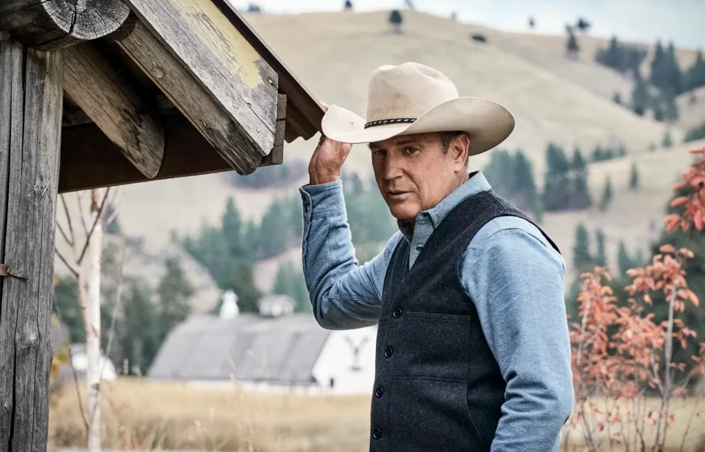 John Dutton (Kevin Costner) looks out from under a wooden structure.