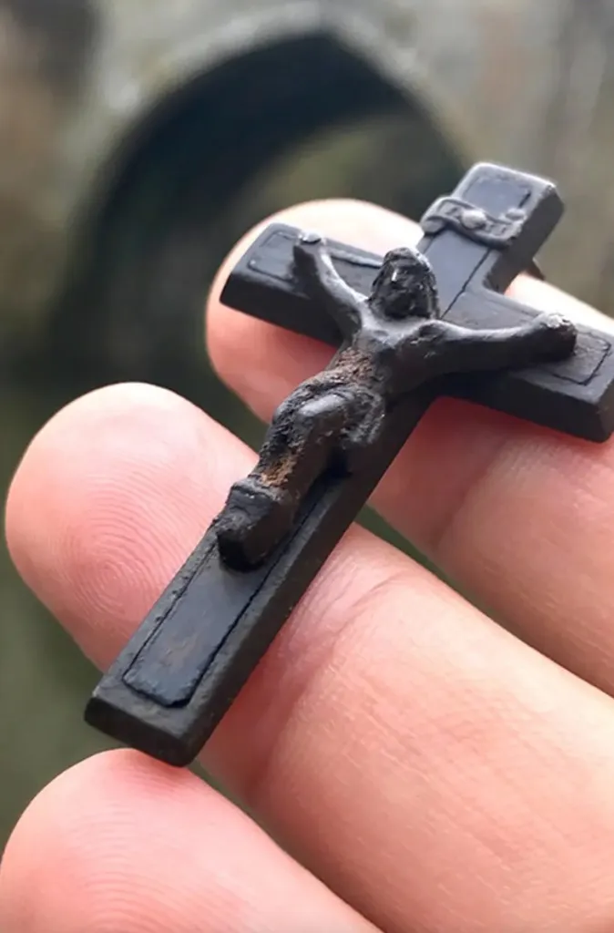Bronze crucifix found in a river, held between two fingers.