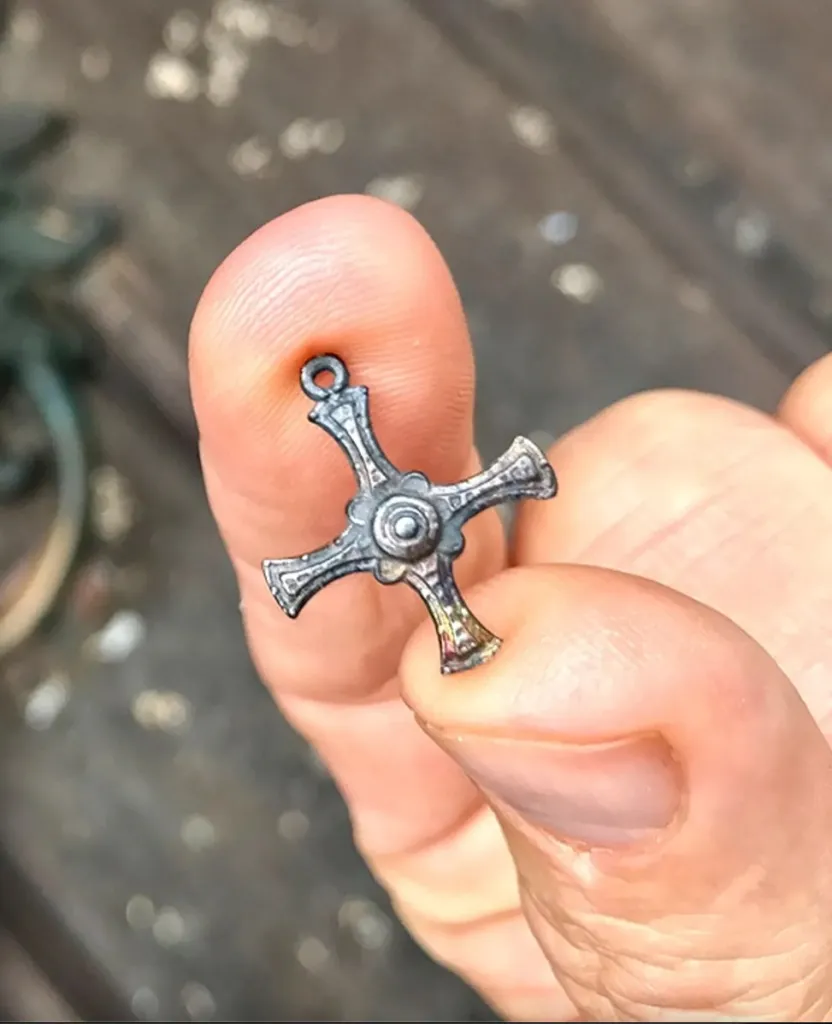 A small, ornate bronze crucifix held between two fingers.