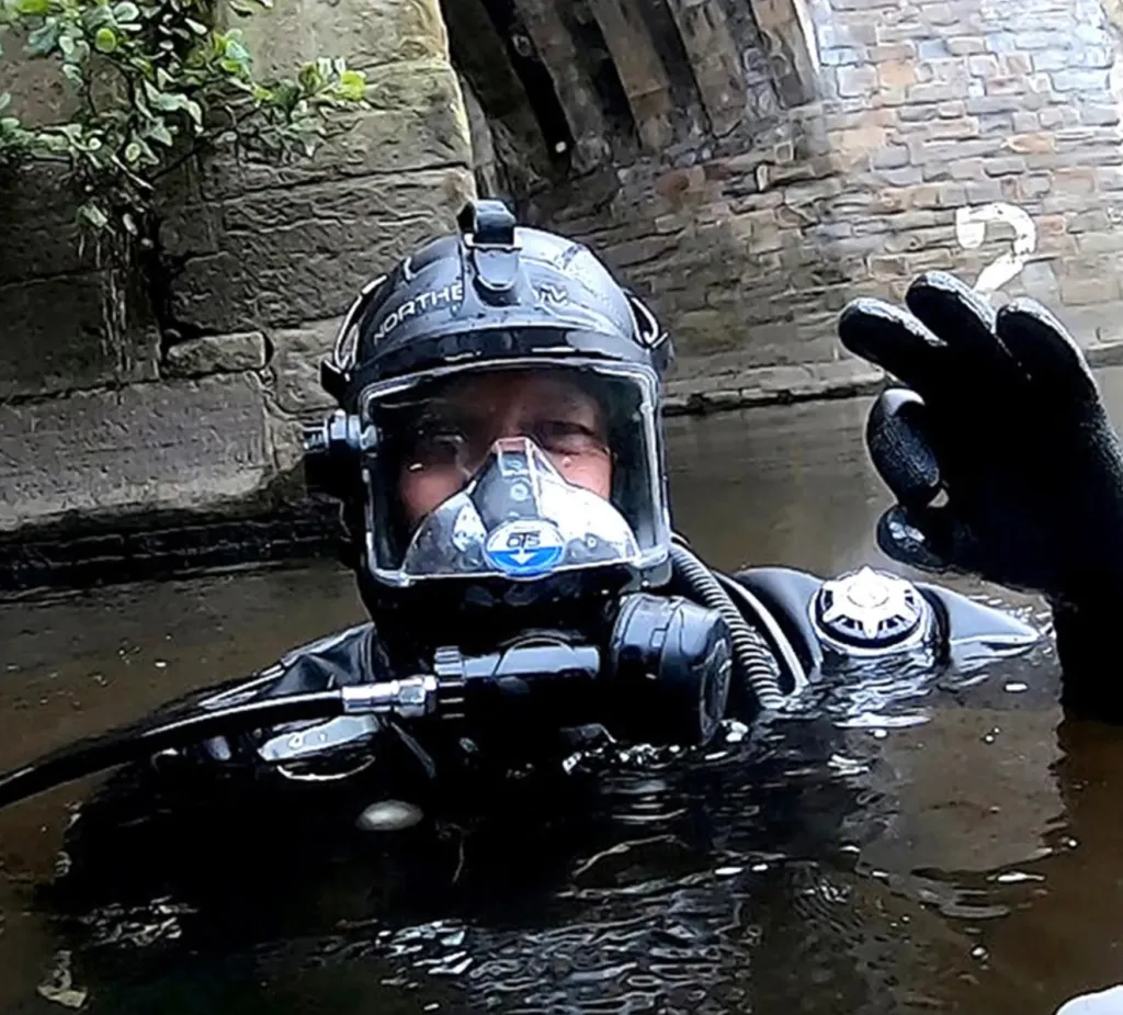 An archaeologist in diving gear holds up a crucifix found in the River Wear.