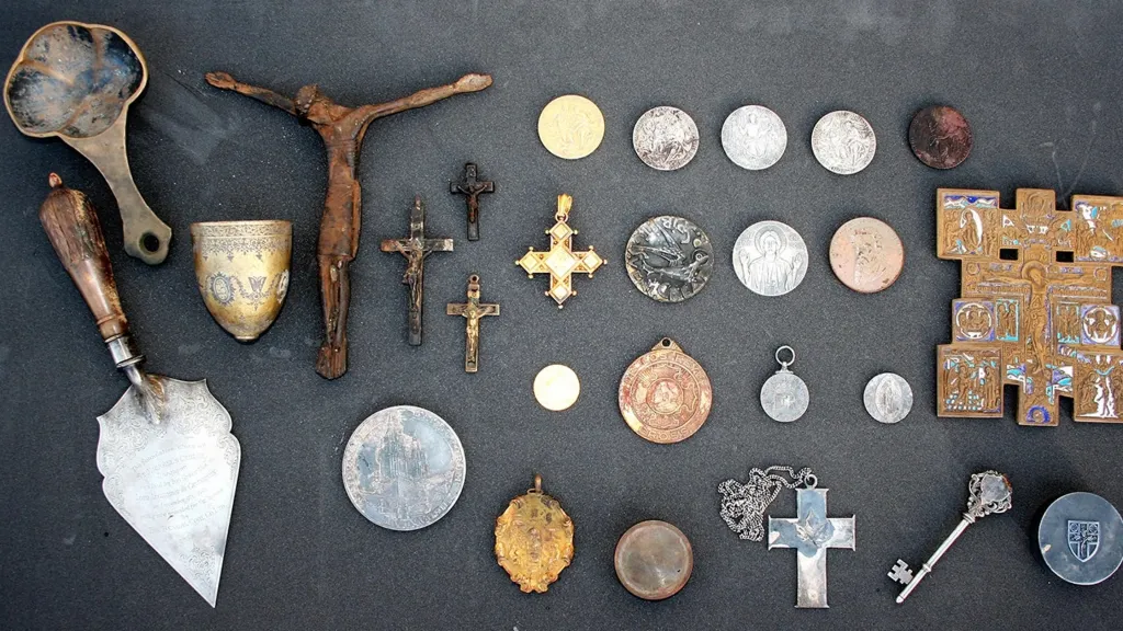 A collection of religious artifacts, including crucifixes, coins, medals, a silver trowel, and a spoon.