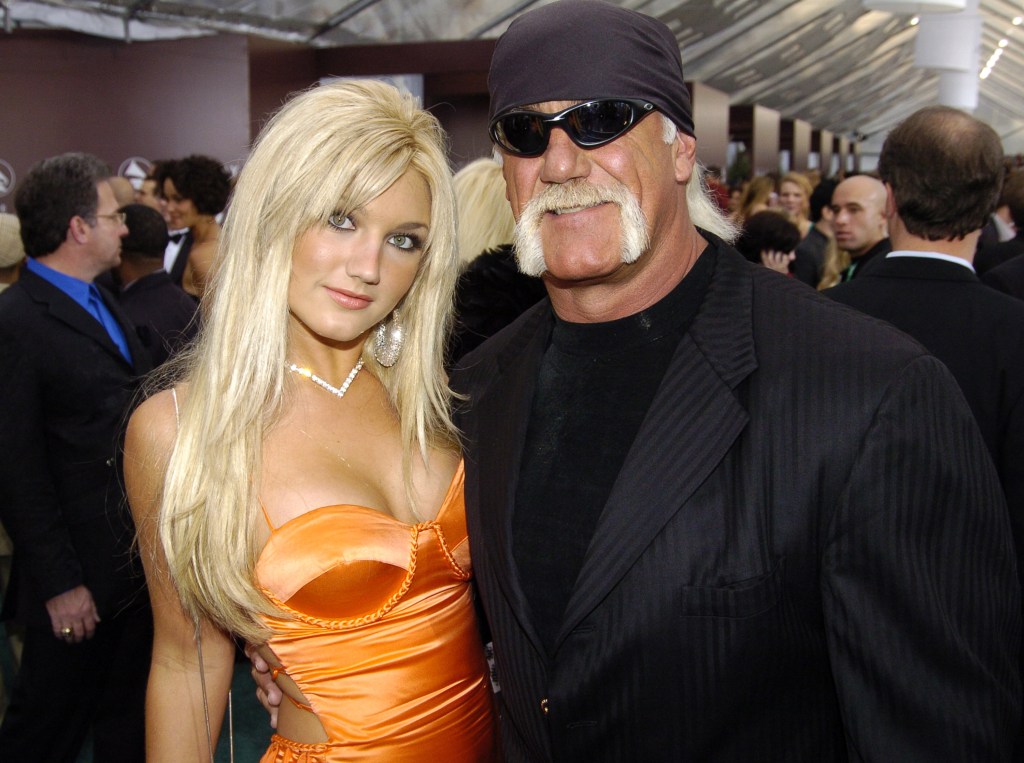 Brooke Hogan in an orange dress and Hulk Hogan in a black bandana and black suit.