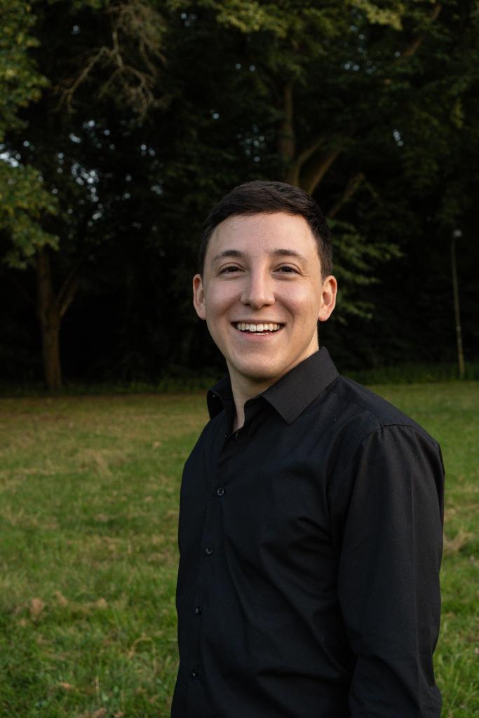 Smiling man with short dark hair in a black shirt in a park.