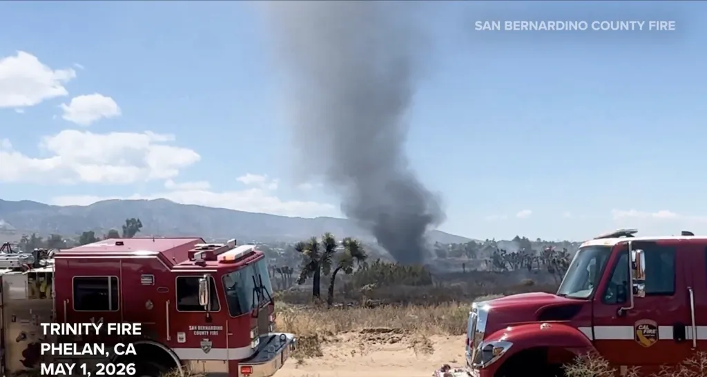 An ash devil rises from a wildfire in San Bernardino County, with two fire trucks in the foreground.