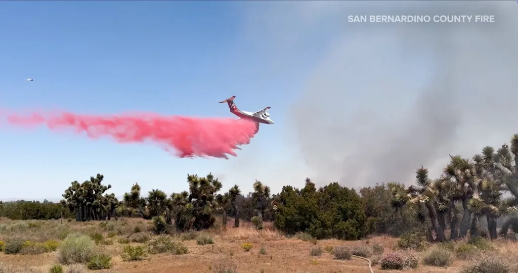 A firefighting plane dropping red retardant over a wildfire in a desert landscape.