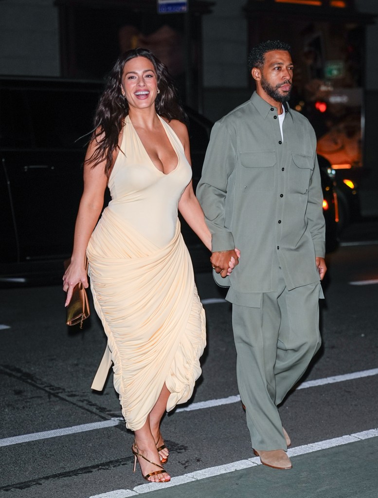 Ashley Graham in a peach halter dress and Justin Ervin in an olive green suit walk hand-in-hand.