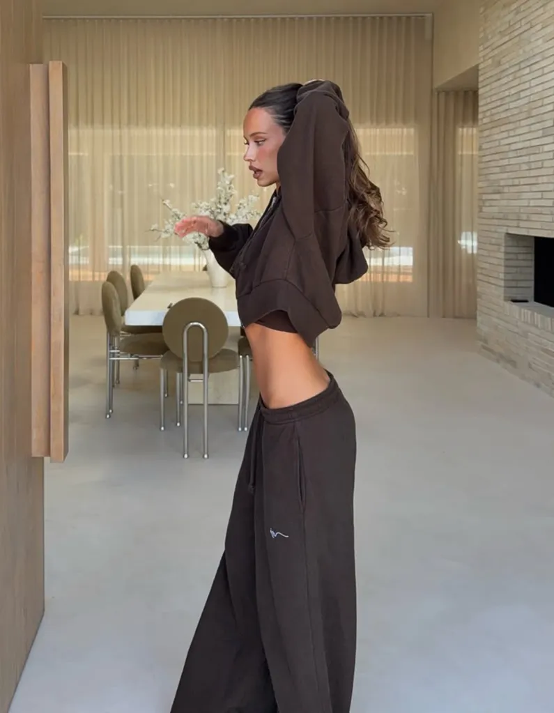Isabelle Mathers showing her midriff in a brown hooded top and sweatpants, with a dining area in the background.