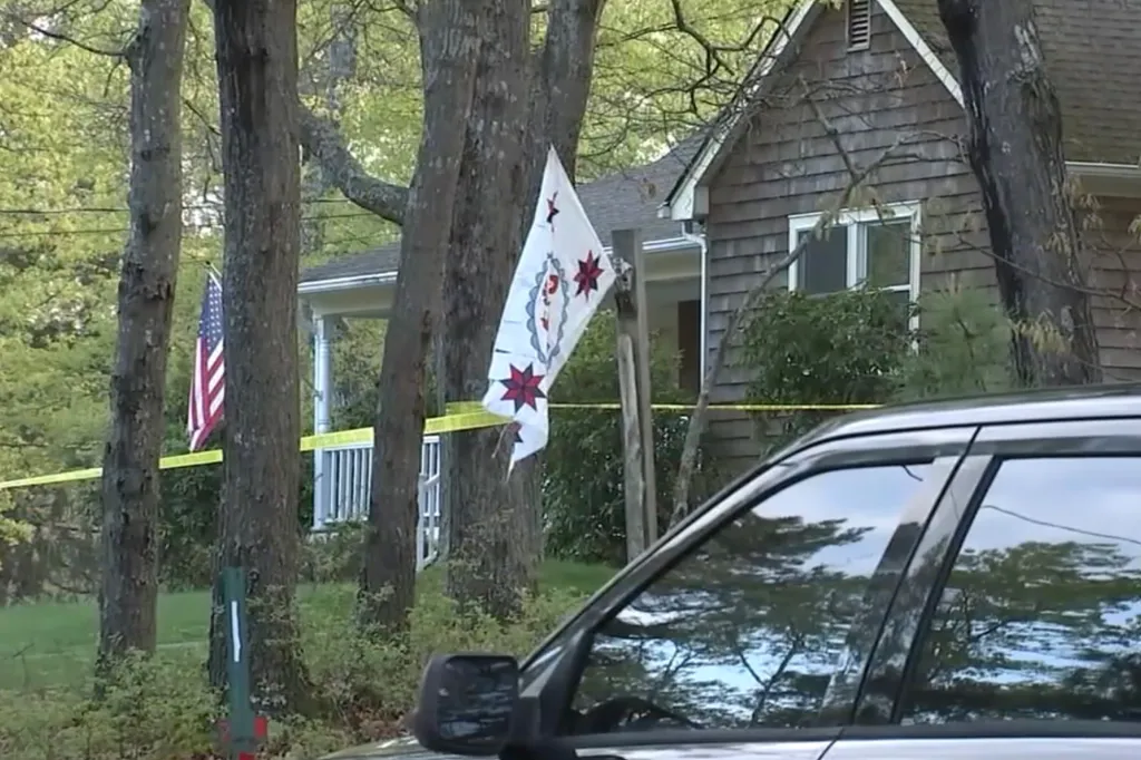 A police car parked outside a house with yellow crime scene tape across the lawn.