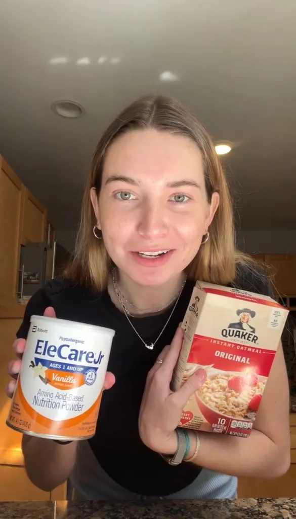 Caroline Cray holding a can of EleCare Jr. vanilla amino acid-based nutrition powder and a box of Quaker original instant oatmeal.