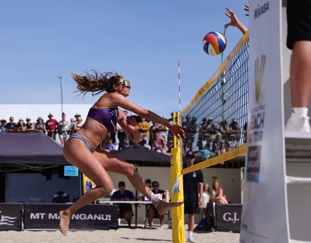 Avery Poppinga jumping to hit the volleyball over the net during the World Beach Volleyball Pro Tour.