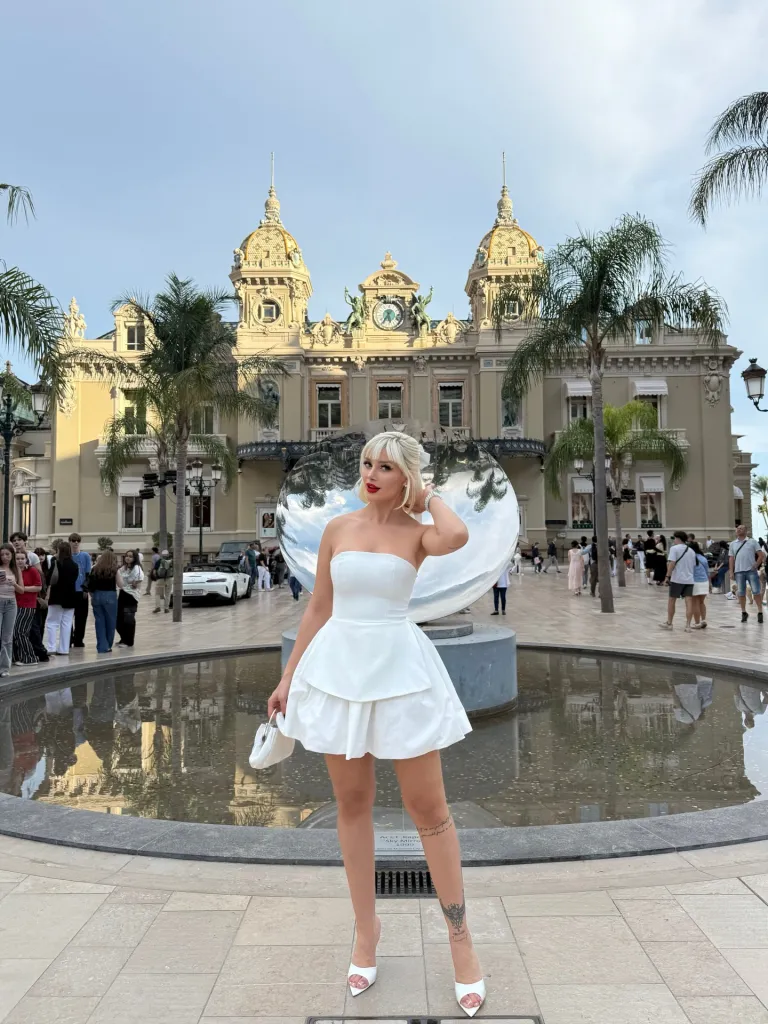 Aysegul Eraslan in a white dress posing in front of the Monte Carlo Casino.