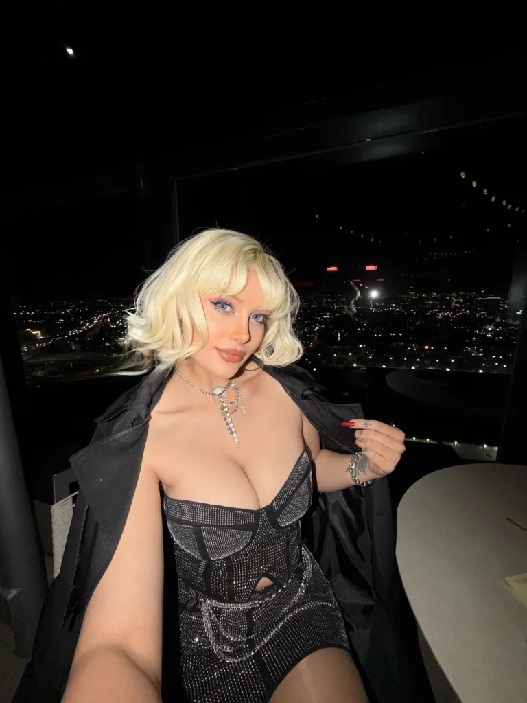 Ayşegül Eraslan in a sparkly black dress and jacket, wearing a necklace, posing in front of a city night view.