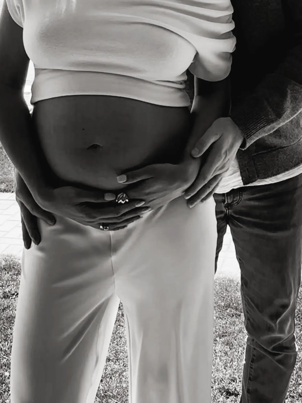 A black and white photo of a couple's hands caressing a pregnant belly.