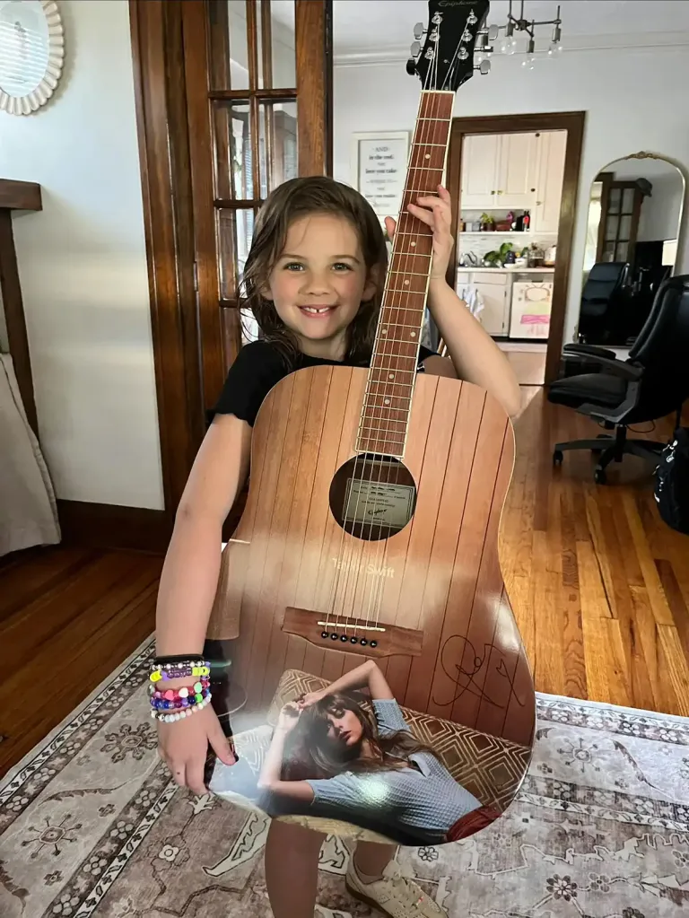 An 8-year-old girl holding a Taylor Swift guitar.