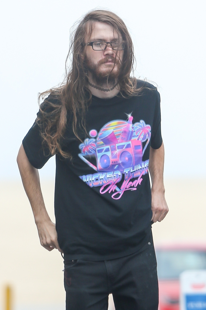Chance Hogan walking in Venice Beach wearing a black t-shirt, black pants, glasses, and a choker necklace.