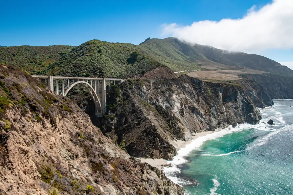 Bixby Creek Bridge on Highway 1, California, spans a gorge with cliffs dropping to a beach and the Pacific Ocean.