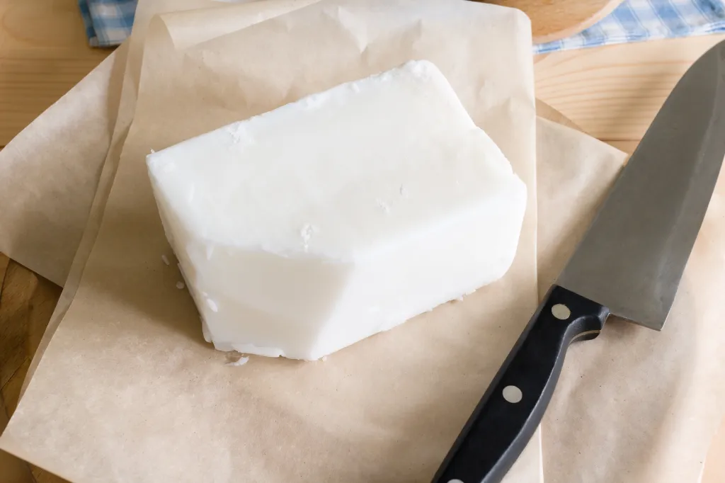 A block of white tallow or beef dripping on brown parchment paper with a chef's knife beside it.